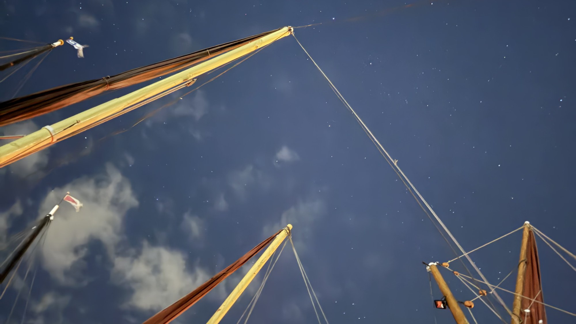 Masts and rigging of sailing barges reaching up into a starry night sky